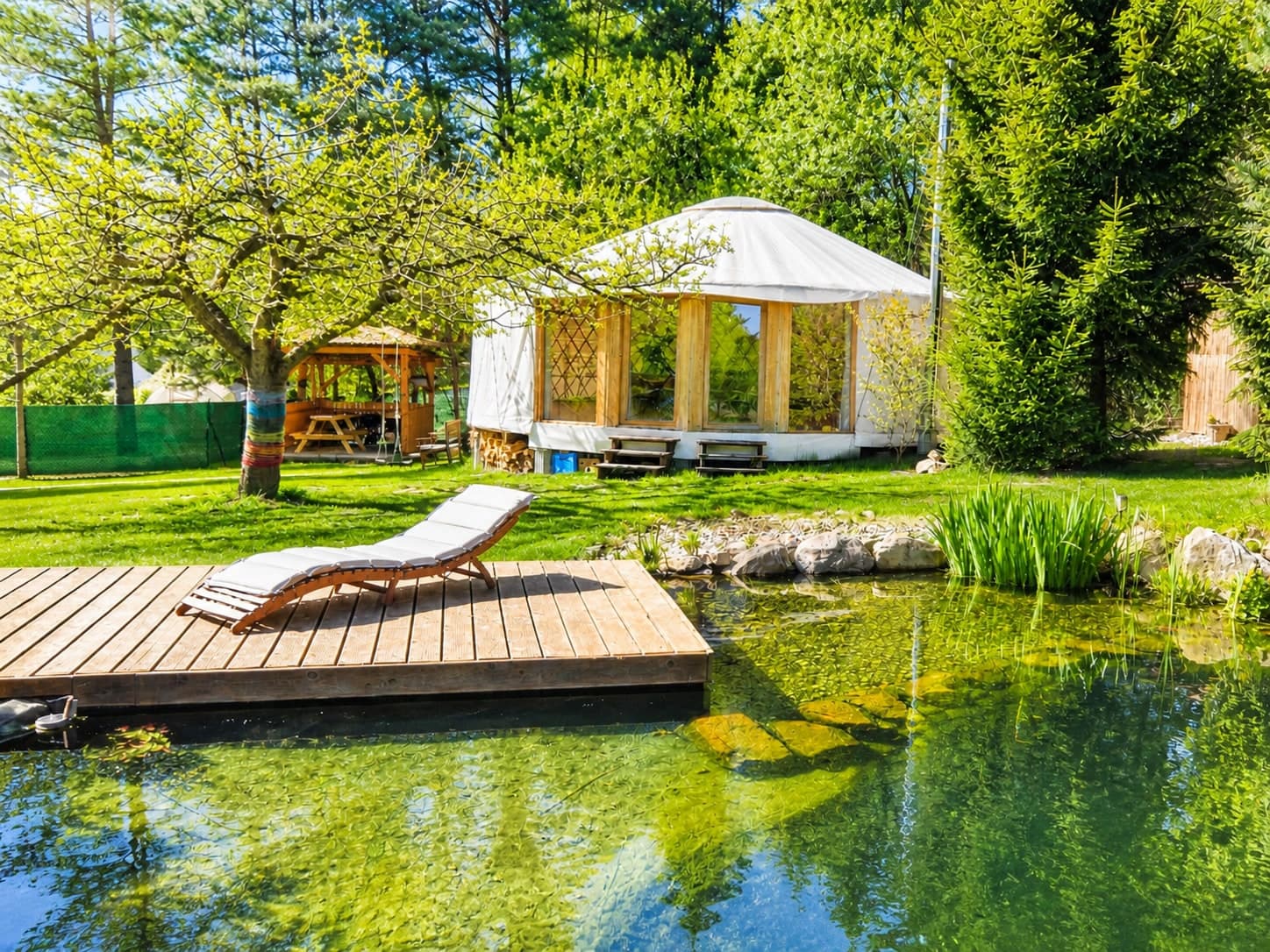 Velká jurta s lehátkem na dřevěném molu nad přírodním jezírkem — glamping Podkrkonoší